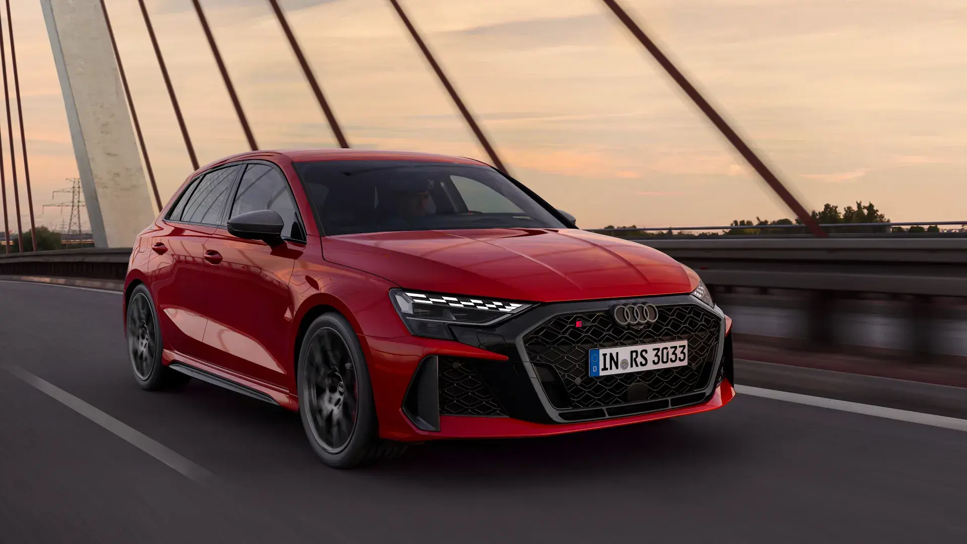 Rød Audi RS 3 kører over en bro i aftensolen.