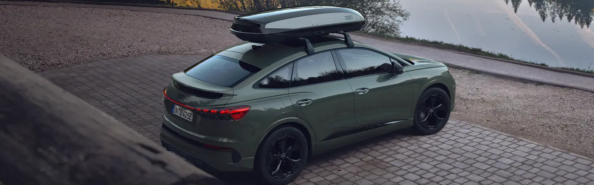 Grøn SUV parkeret ved en sø med en tagboks monteret på tagbøjlerne.