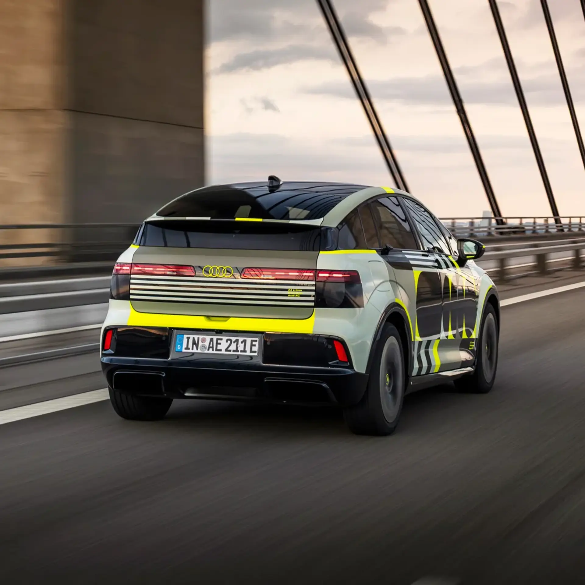 En moderne Audi elbil med camouflagefolie kører over en bro i høj fart.